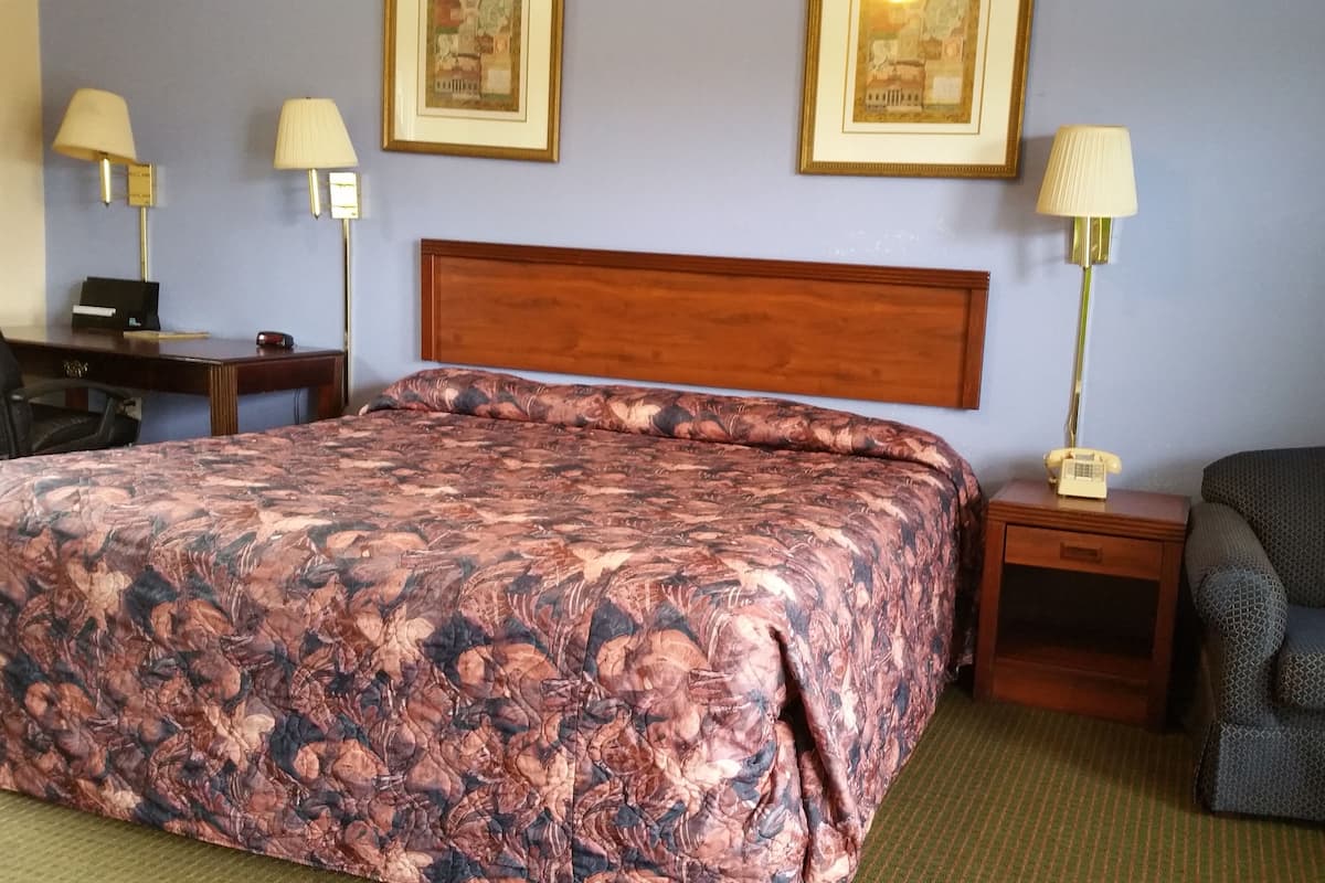 A hotel room with a large bed, a desk, two bedside tables with lamps, a chair, and two framed pictures on the wall.