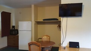 Eine kompakte Küche mit Kühlschrank, Mikrowelle und einem kleinen Esstisch mit Stühlen. Ein Flachbildfernseher ist an der Wand über der Arbeitsfläche angebracht.