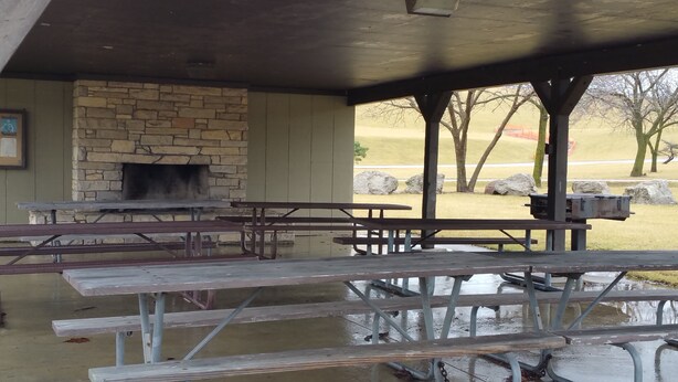 Ein Pavillon im Freien mit Steinwänden, Kamin und Picknicktischen.