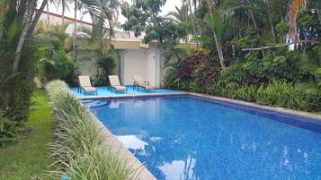 Relax by the serene pool surrounded by lush tropical vegetation and three sun loungers.