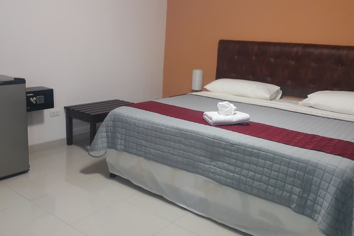 A hotel room with a bed, a small desk, and a refrigerator.