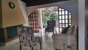 A room with a sofa, a floral armchair, a glass coffee table, a clock on the wall, and a view through an arched doorway to an outdoor area with plants. - Hotel Portal Colonial (San Rafael)