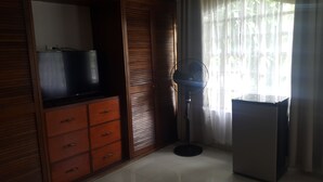 A room with a TV on a wooden cabinet, a standing fan, and a refrigerator. - Hotel Portal Colonial (San Rafael)