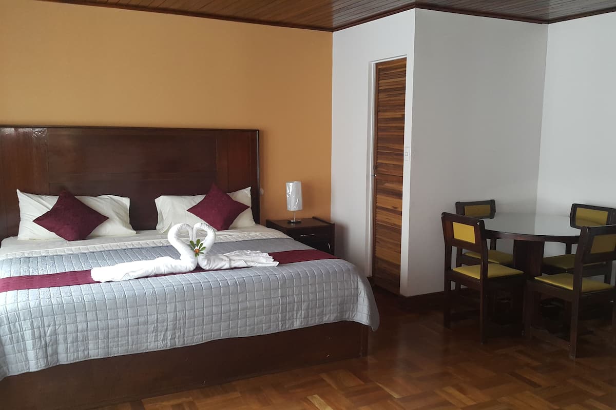 A hotel room with a bed, a nightstand, a desk with two chairs, and a wooden door.