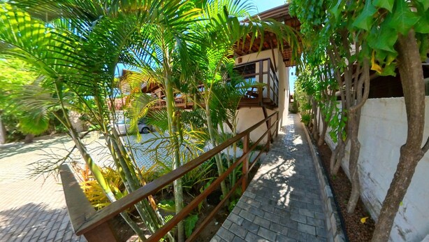 A pathway lined with greenery and a building with a balcony. - Pousada Mar e Brisa (Natal)