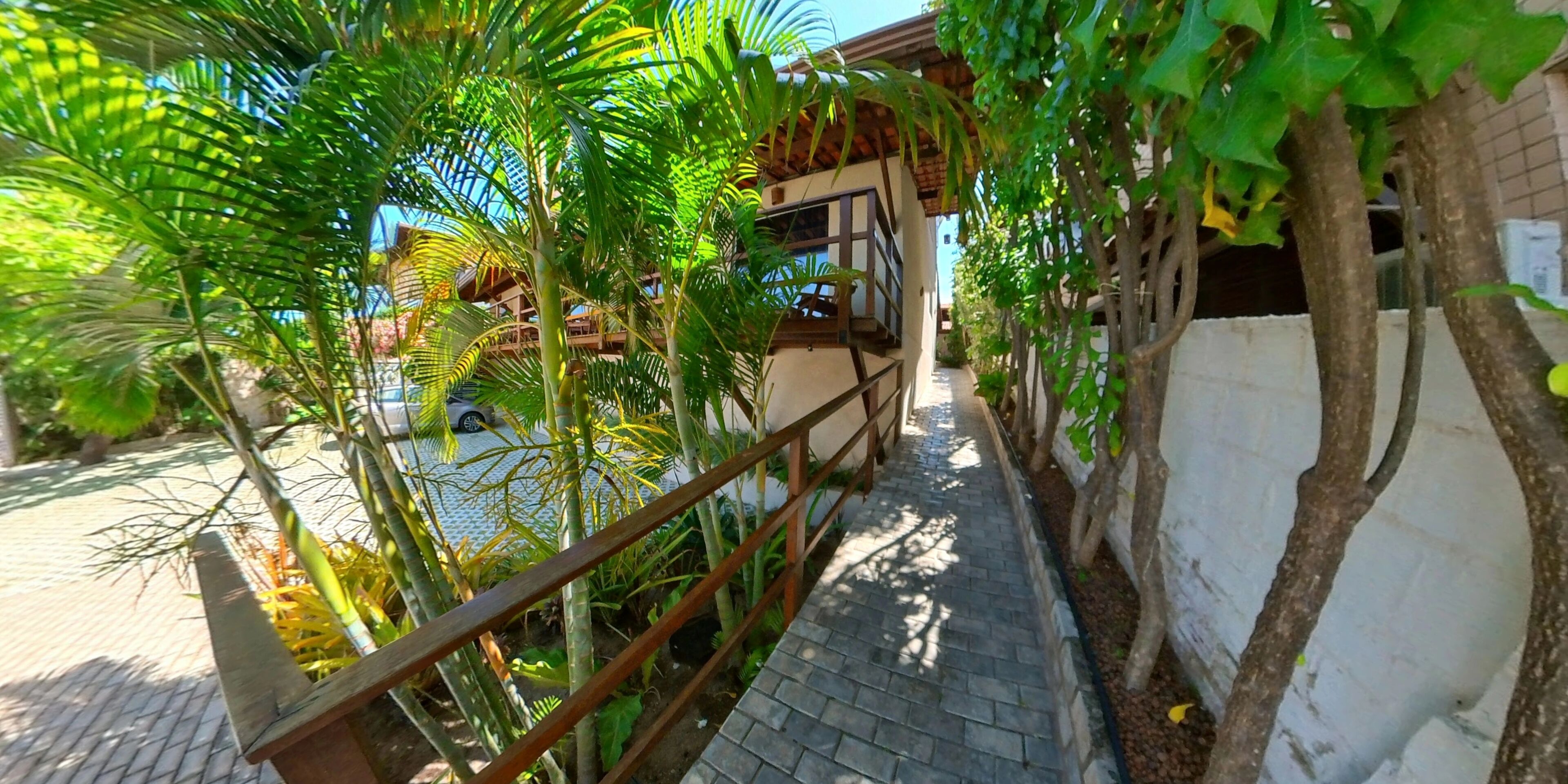 A pathway lined with greenery and a building with a balcony. - Pousada Mar e Brisa (Natal)
