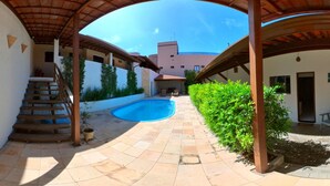 A covered outdoor area with a swimming pool, stairs, and a building in the background. - Pousada Mar e Brisa (Natal)
