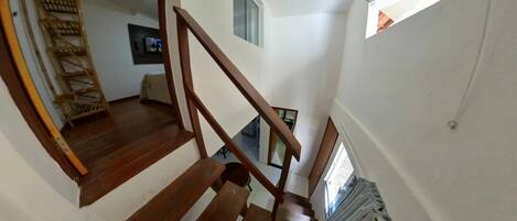 A wooden staircase with a handrail, a wicker chair, and a small table in a room with white walls and a window.