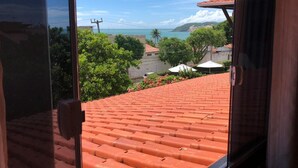 A view from a window overlooking a red-tiled roof, a green landscape, and a distant coastline. - Pousada Mar e Brisa (Natal)