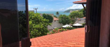 A view from a window overlooking a red-tiled roof, a green landscape, and a distant coastline.