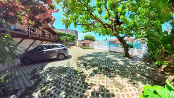 A car parked on a patterned pavement with a tree and greenery in the foreground.