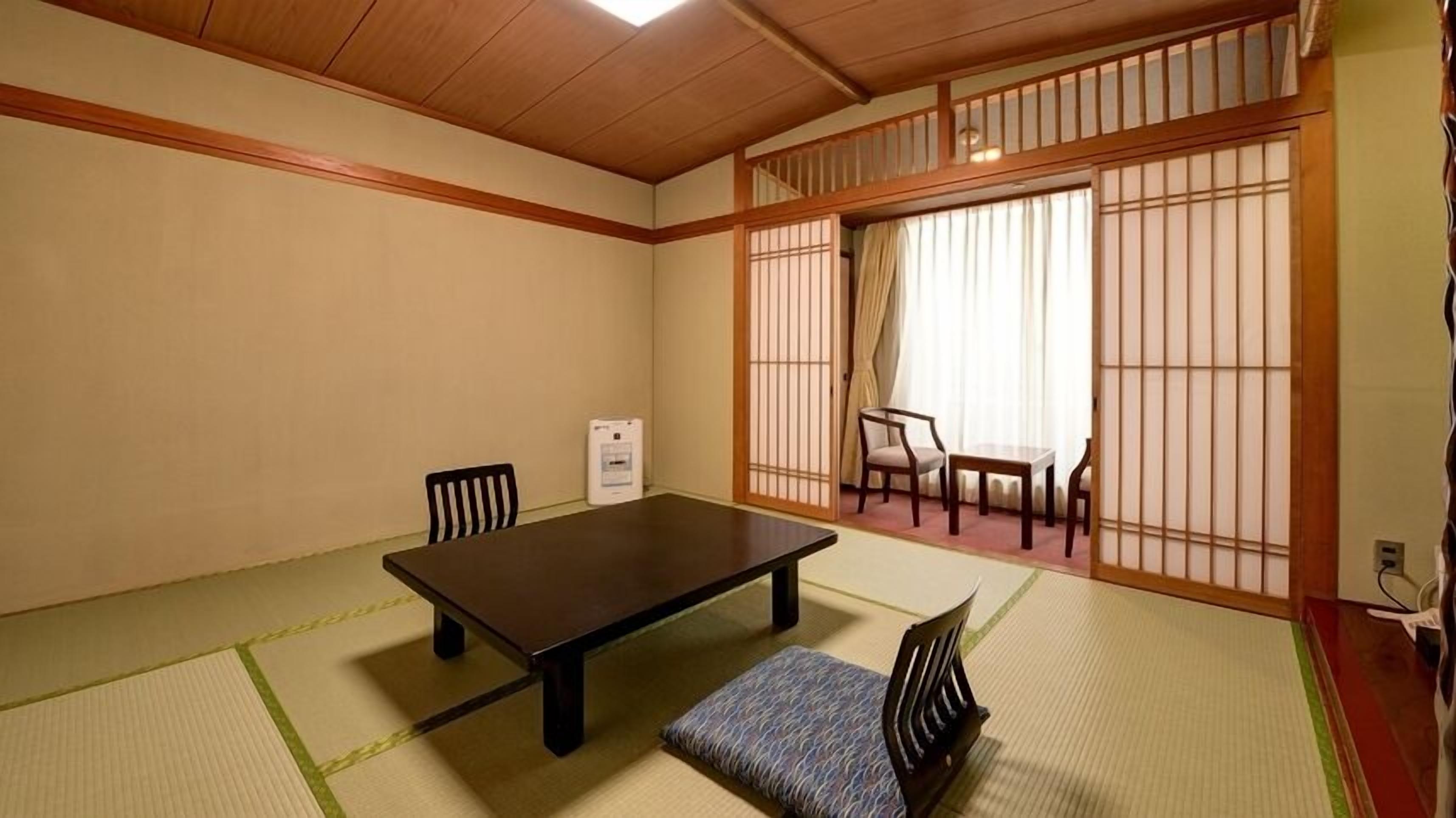 Una habitación japonesa tradicional con suelo de tatami, una mesa baja, sillas y puertas correderas shoji.