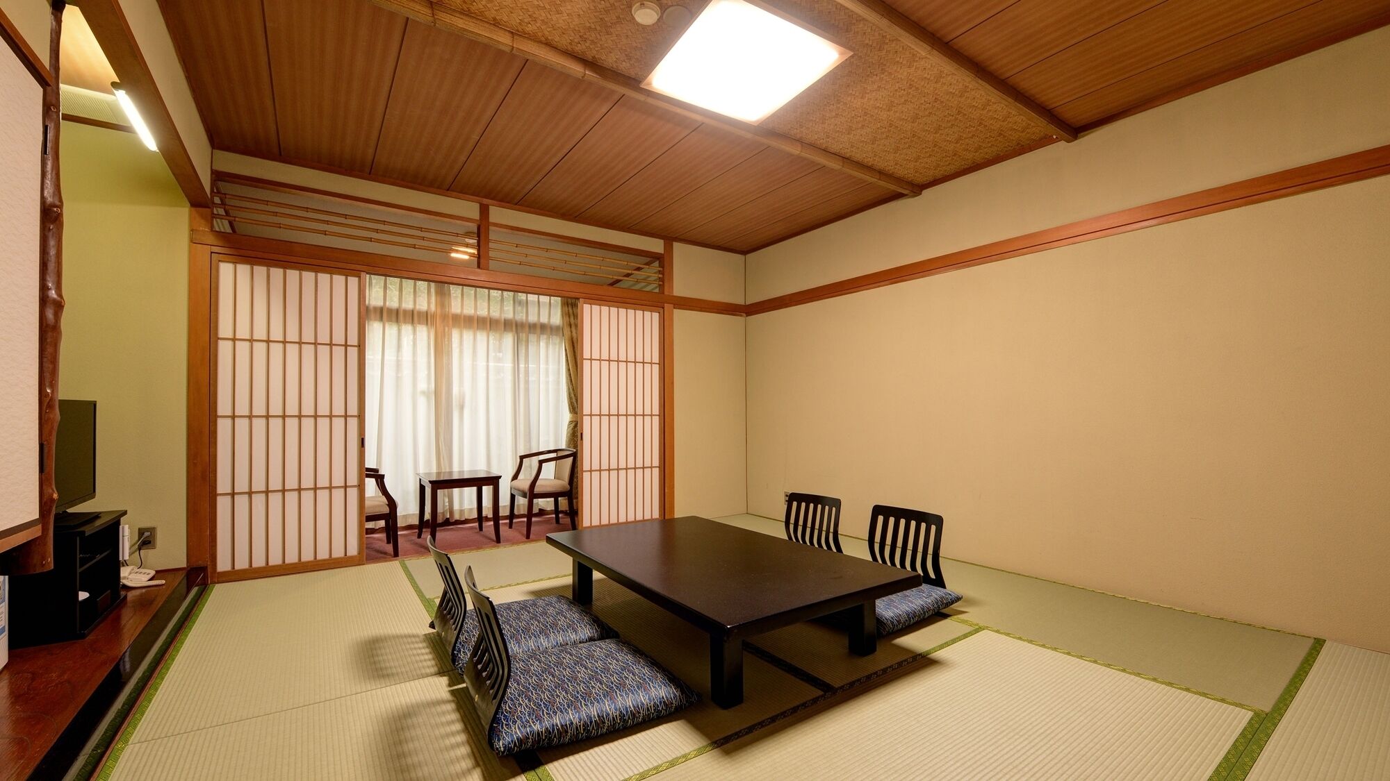 A traditional Japanese room with tatami flooring, a low table with chairs, and sliding doors.