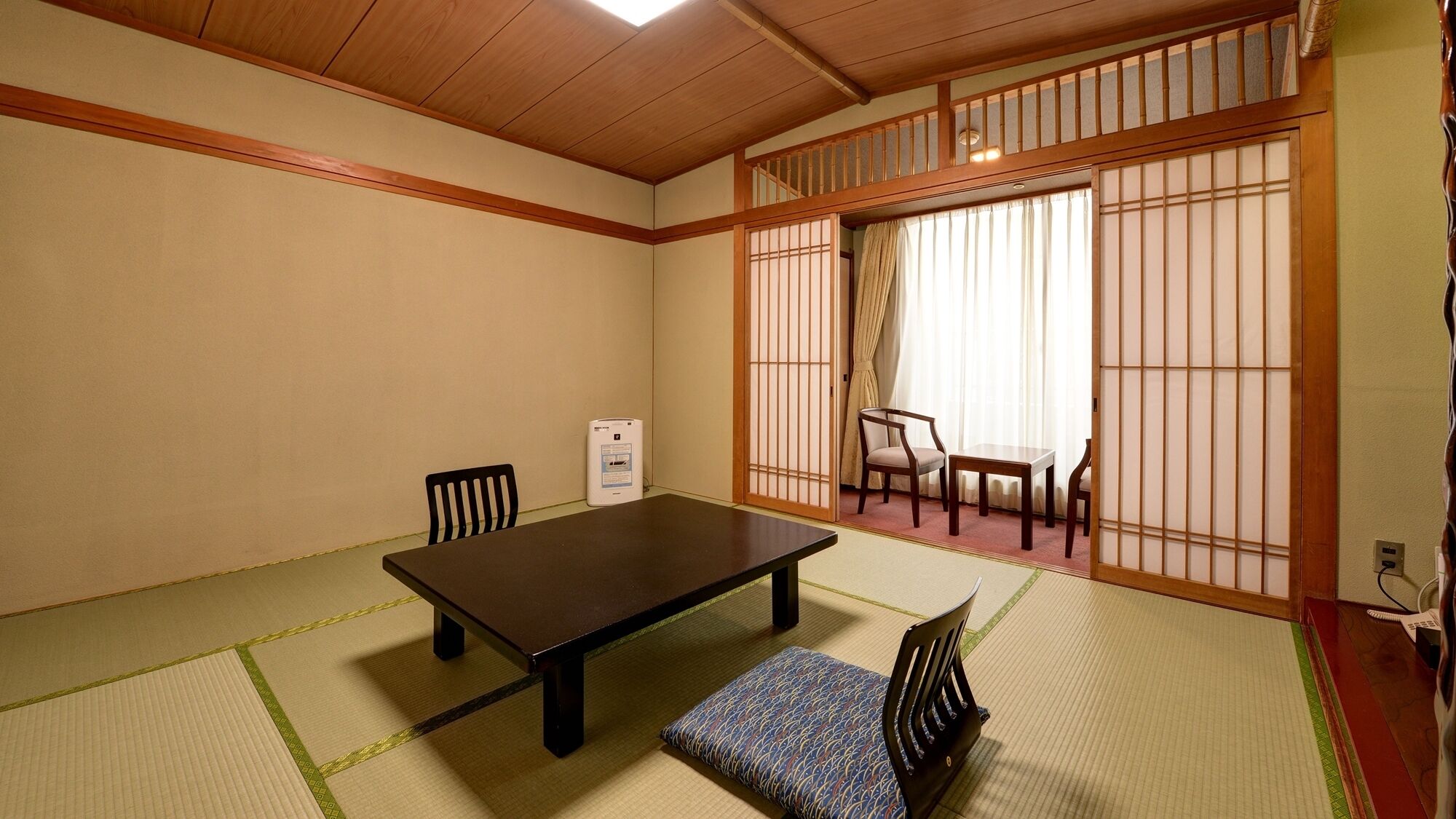 A traditional Japanese room with tatami flooring, a low table, two chairs, and a sliding door with shoji screens.
