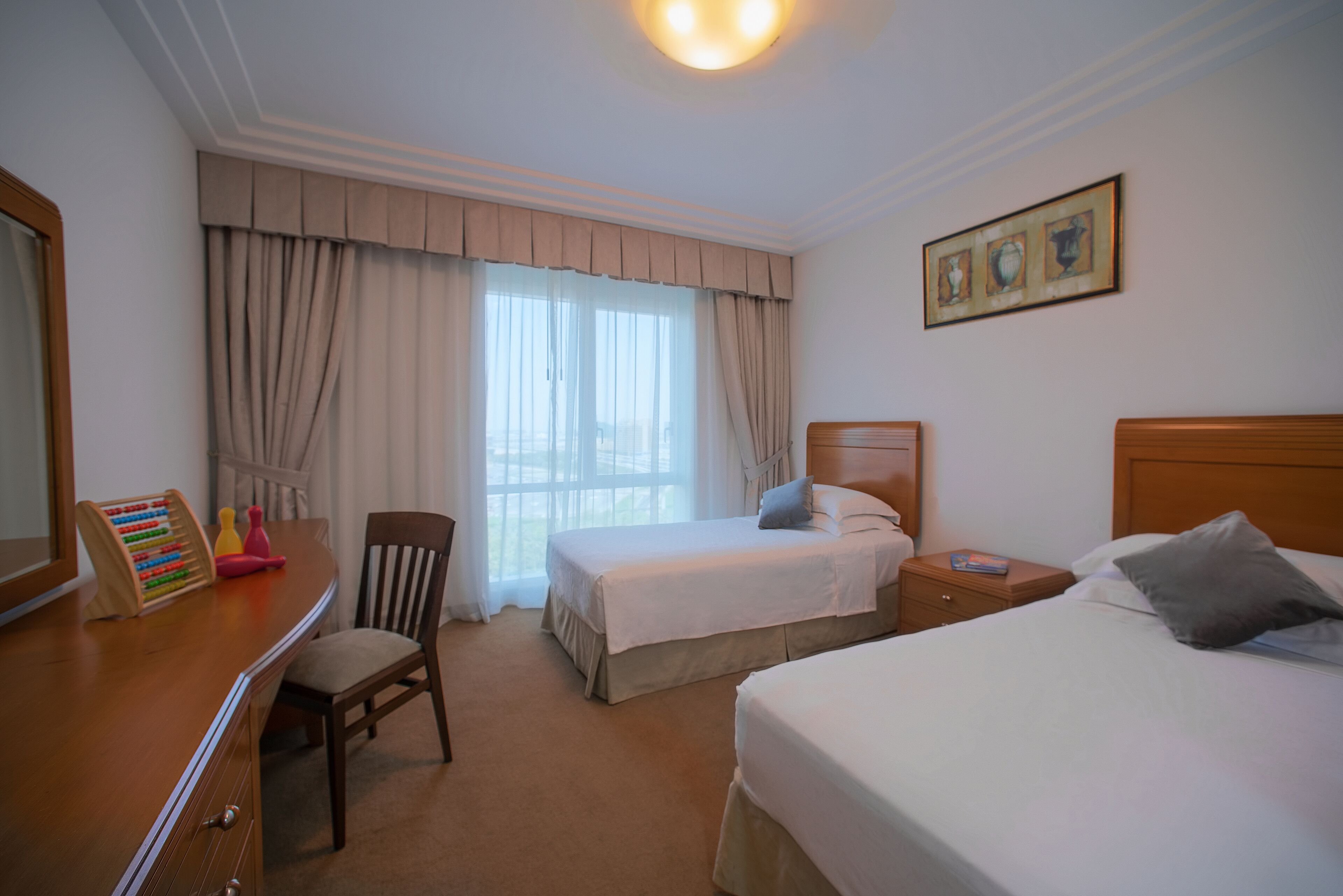 A hotel room with two beds, a desk, a chair, and a window with curtains.