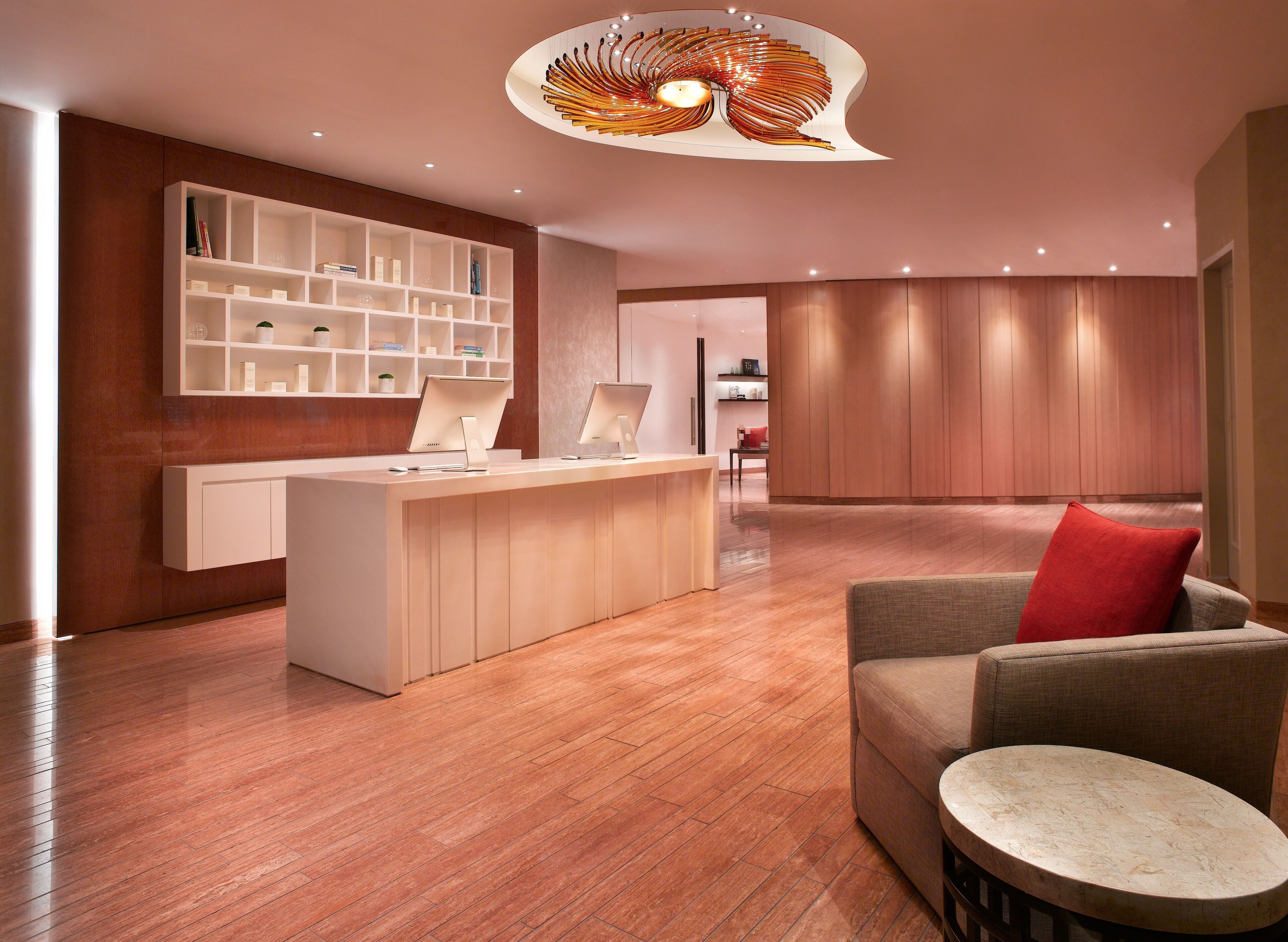 A modern reception area with a wooden reception desk, a white shelving unit, and a unique ceiling light fixture.