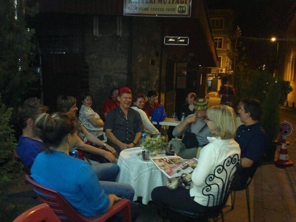 A group of people seated around a table outdoors at night, with a sign above indicating a restaurant.