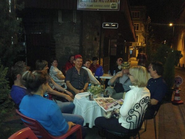 A group of people seated around a table outdoors at night, with a sign above indicating a restaurant.