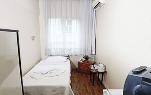 A small, neatly arranged bedroom with a single bed, a bedside table with a lamp, a dresser, and a television. - Sipahi (Istanbul)