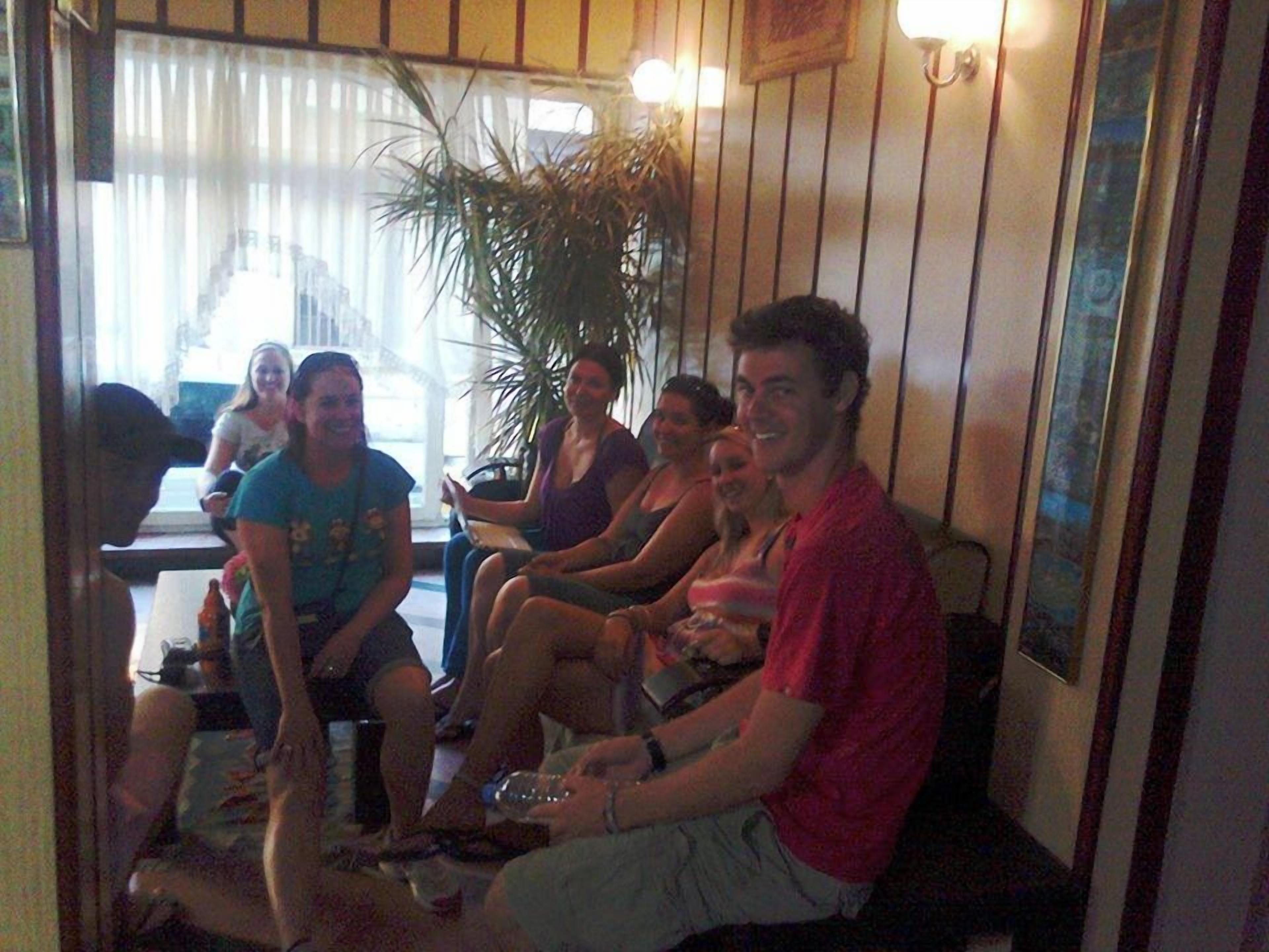 A group of people seated in a room with wooden walls and a large plant.