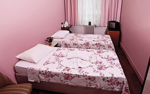 A room with two beds, each with a floral bedspread and white pillows. There is a small table with a lamp, a radiator, and a television on a wooden stand. - Sipahi (Istanbul)