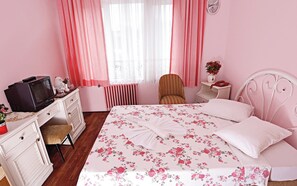 A pink-themed bedroom with a bed, a chair, a dresser, a nightstand, a clock, and a radiator.
