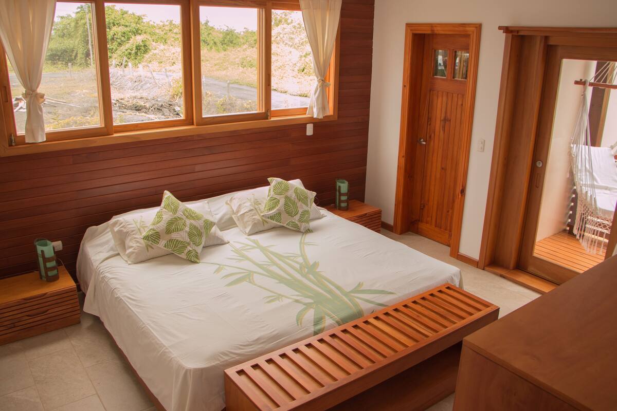 Une chambre à coucher avec un grand lit, une tête de lit en bois et une vue sur l’extérieur par une fenêtre.