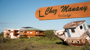 Un letrero de madera que dice 'Chez Manany Ecolodge', indicando un edificio y un bote oxidado.