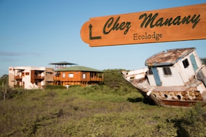 A wooden sign with "Chez Manany Ecolodge" written on it, pointing to a building and a rusted boat.