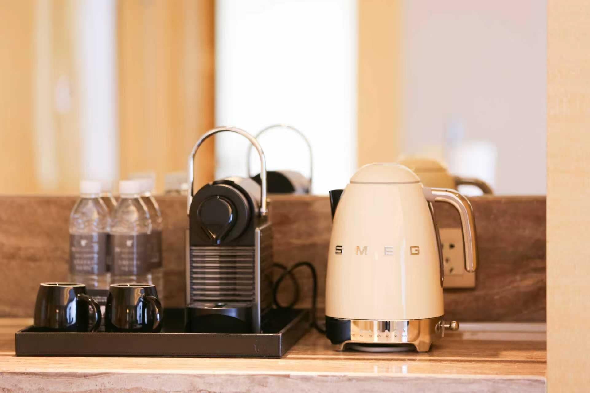 Una encimera de cocina con una cafetera, un hervidor y una bandeja con tazas y un termo.