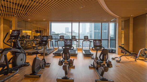 Une salle de sport moderne dotée de nombreux appareils de cardio, de grandes fenêtres et offrant une vue sur la ville.