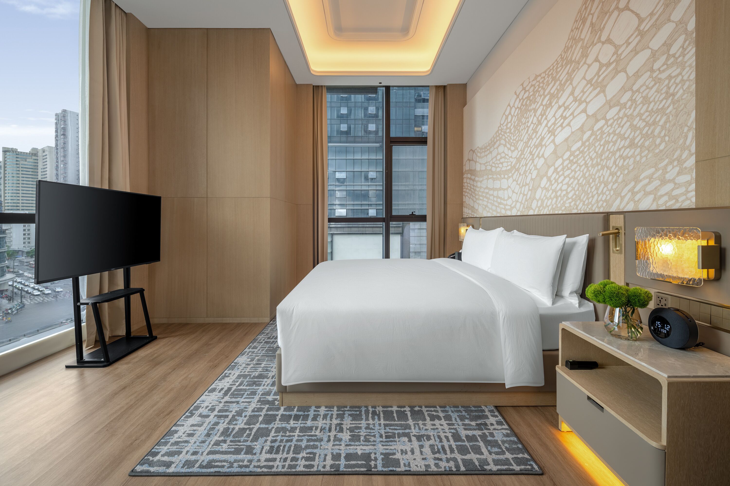 A modern hotel room with a large bed, a TV, and a city view.