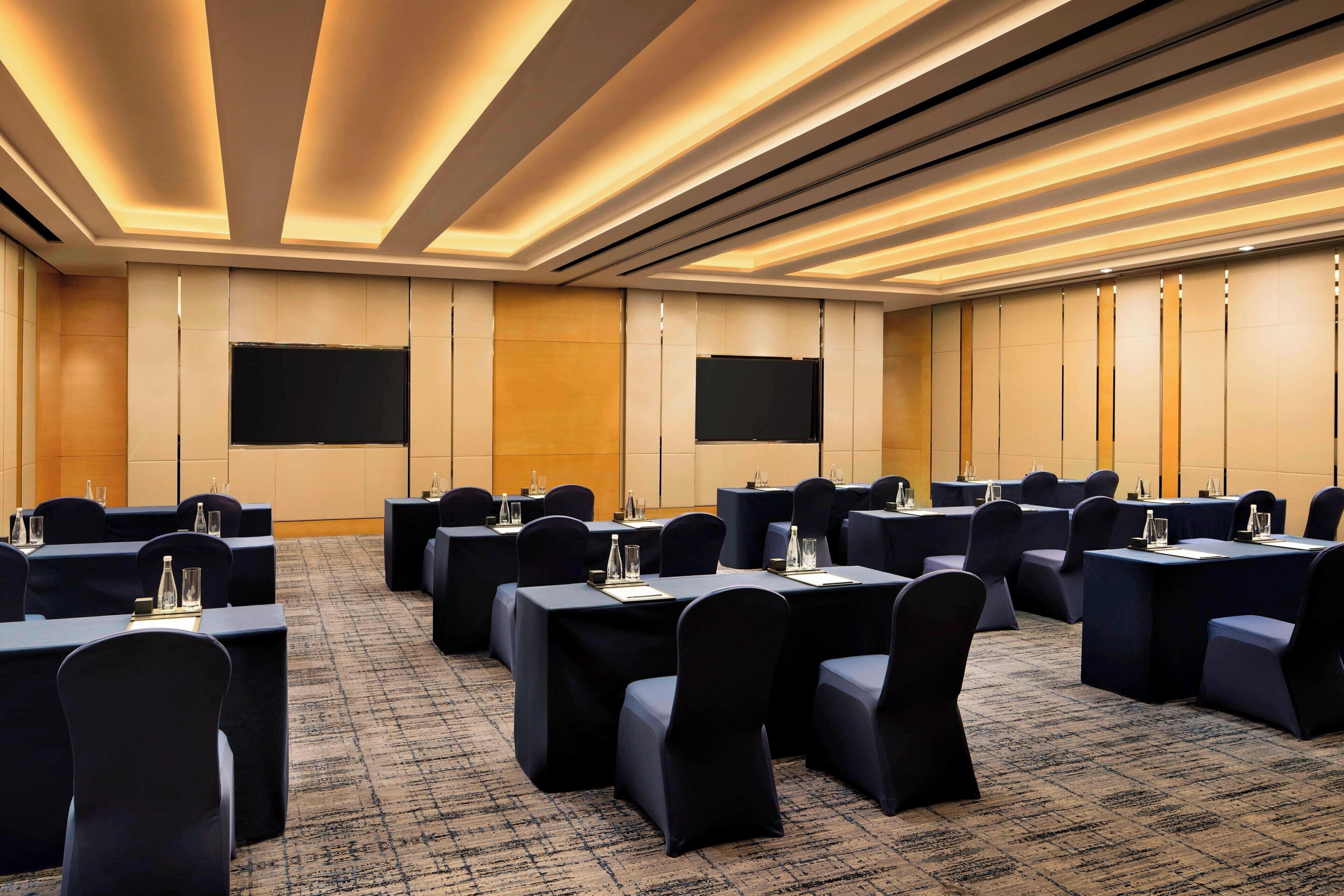 A conference room with multiple tables, chairs, and a large screen.