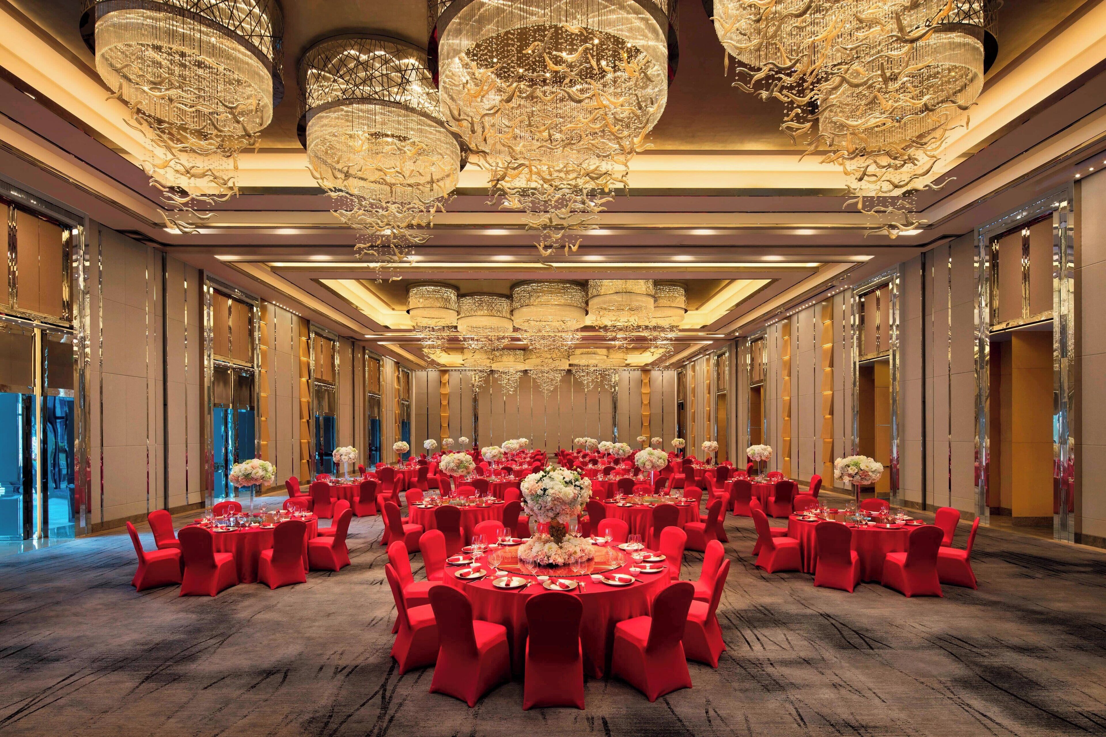 Un salón de banquetes con mesas redondas, sillas rojas y candelabros.