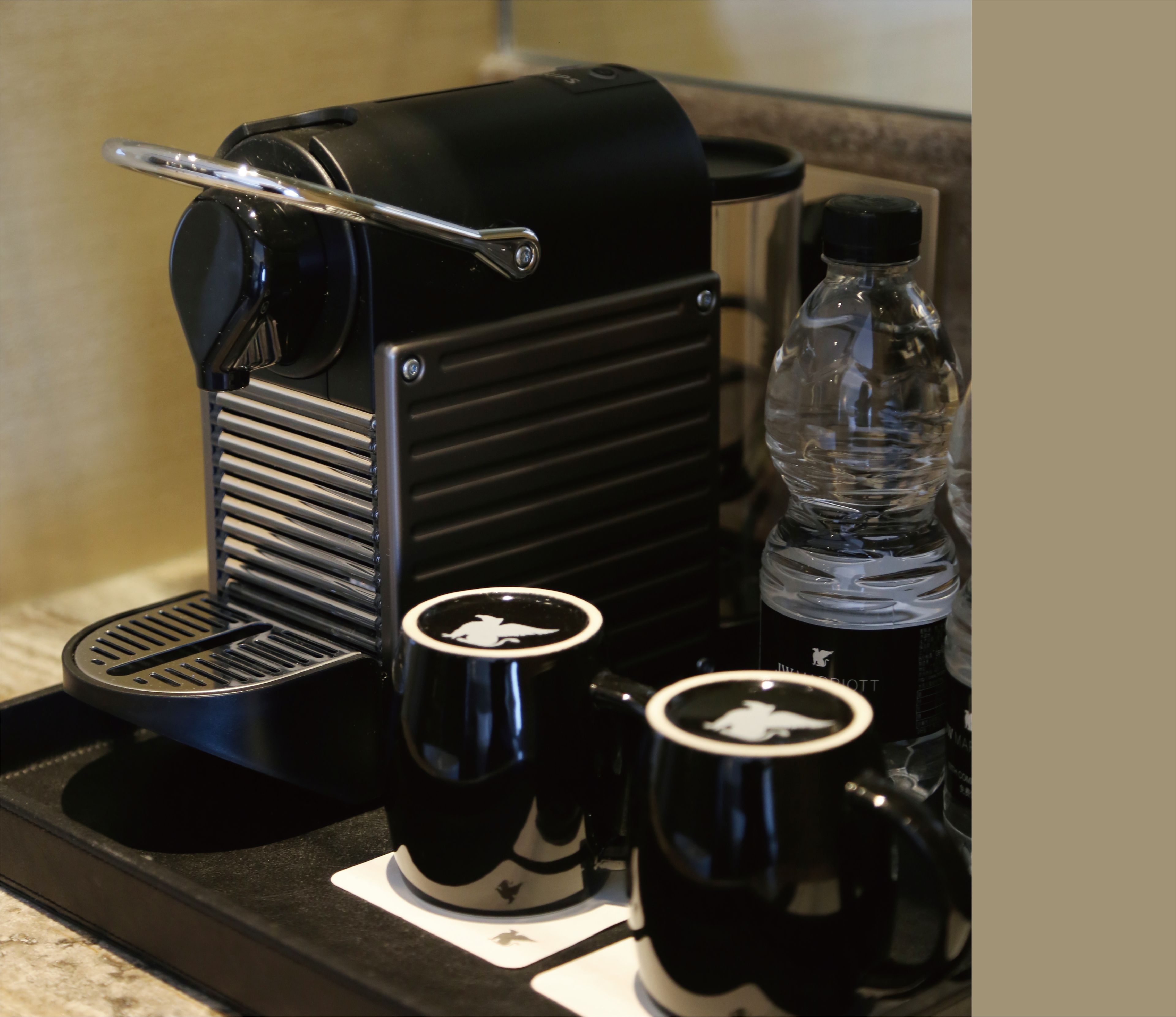 Une machine à café avec deux tasses noires posées sur un plateau.