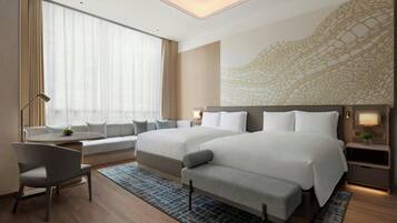 Habitación de hotel moderna con dos camas, un sofá, zona de comedor y un ventanal con cortinas translúcidas.
