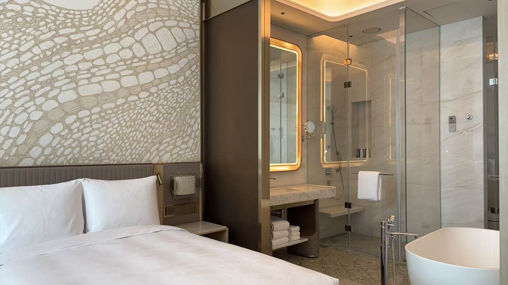 Een moderne hotelkamer met een groot bed, een badkamer met een douchecabine van glas en een wand met een stenen patroon.
