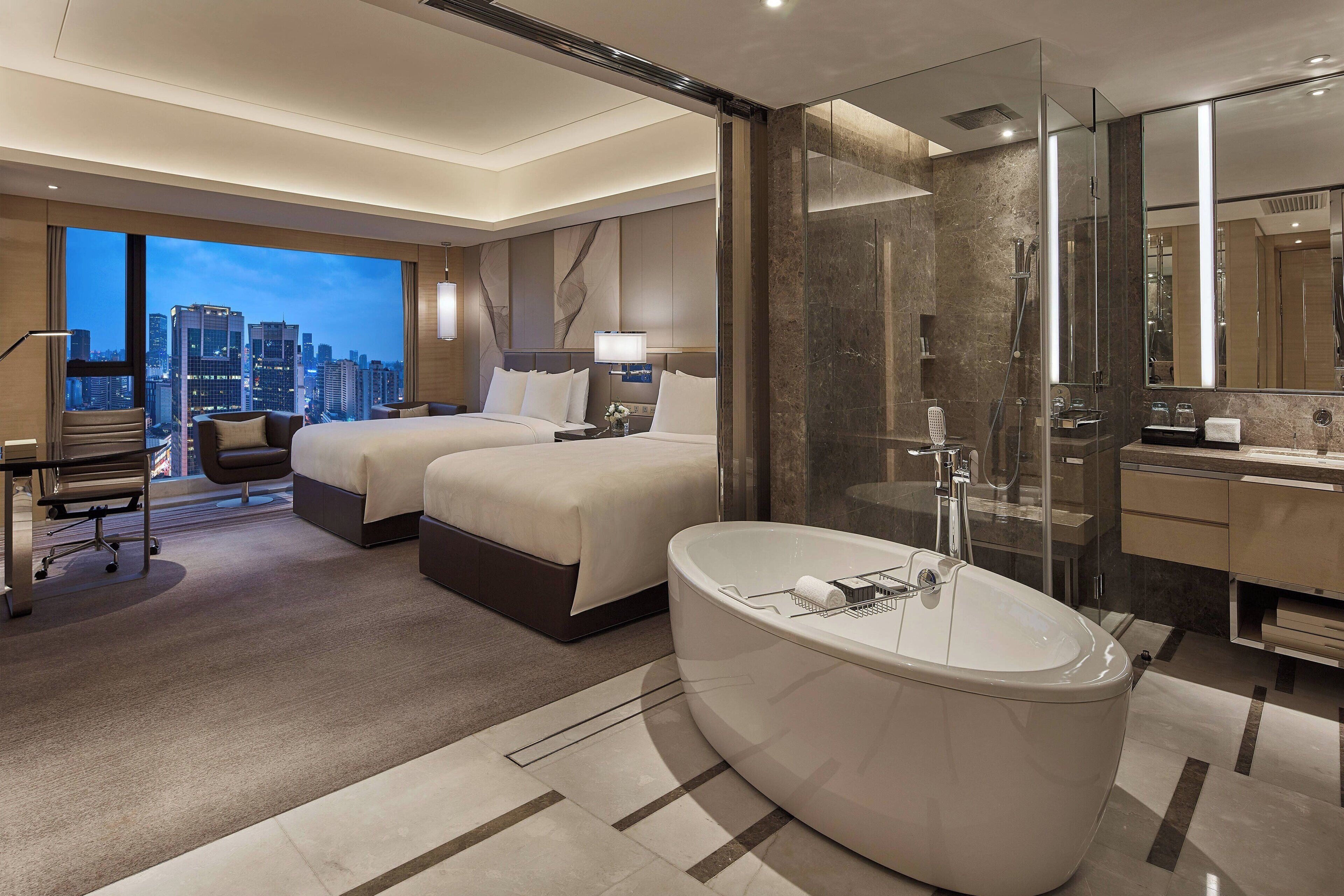 Ein modernes Hotelzimmer mit einem großen Bett, einer separaten Sitzecke, einer großen Badewanne und Blick auf die Stadt.