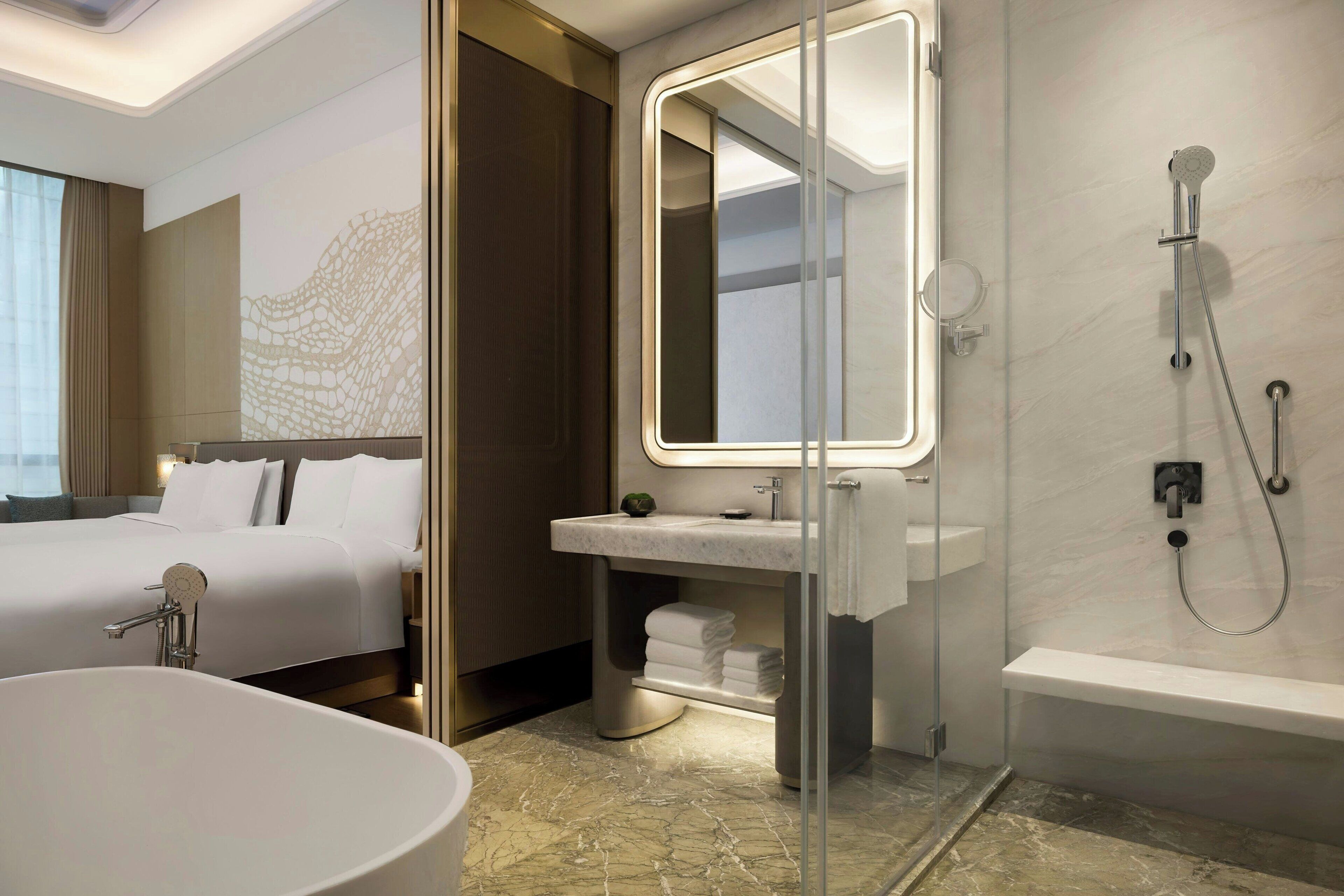 Une salle de bain d’hôtel moderne, dotée d’une grande baignoire, d’une douche à parois de verre et d’un meuble-lavabo avec un miroir.