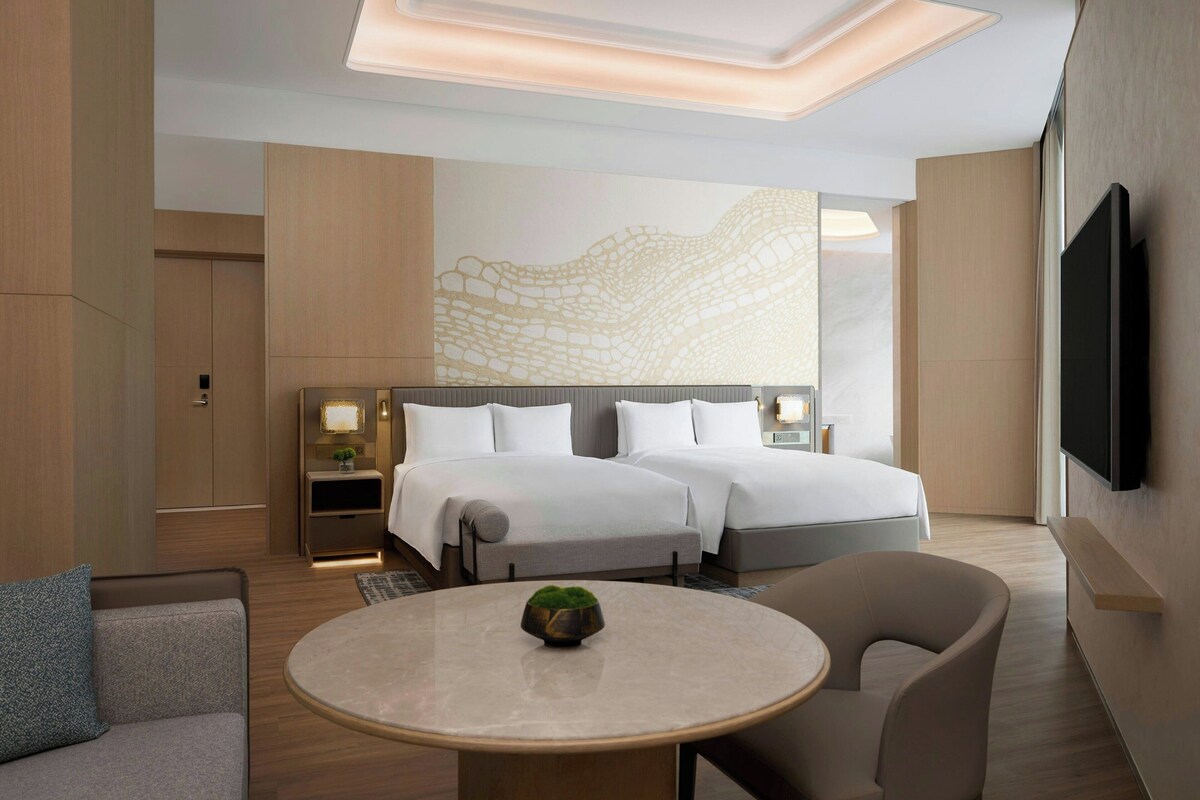 A modern hotel room with a large bed, a TV, a round table, and a sofa.