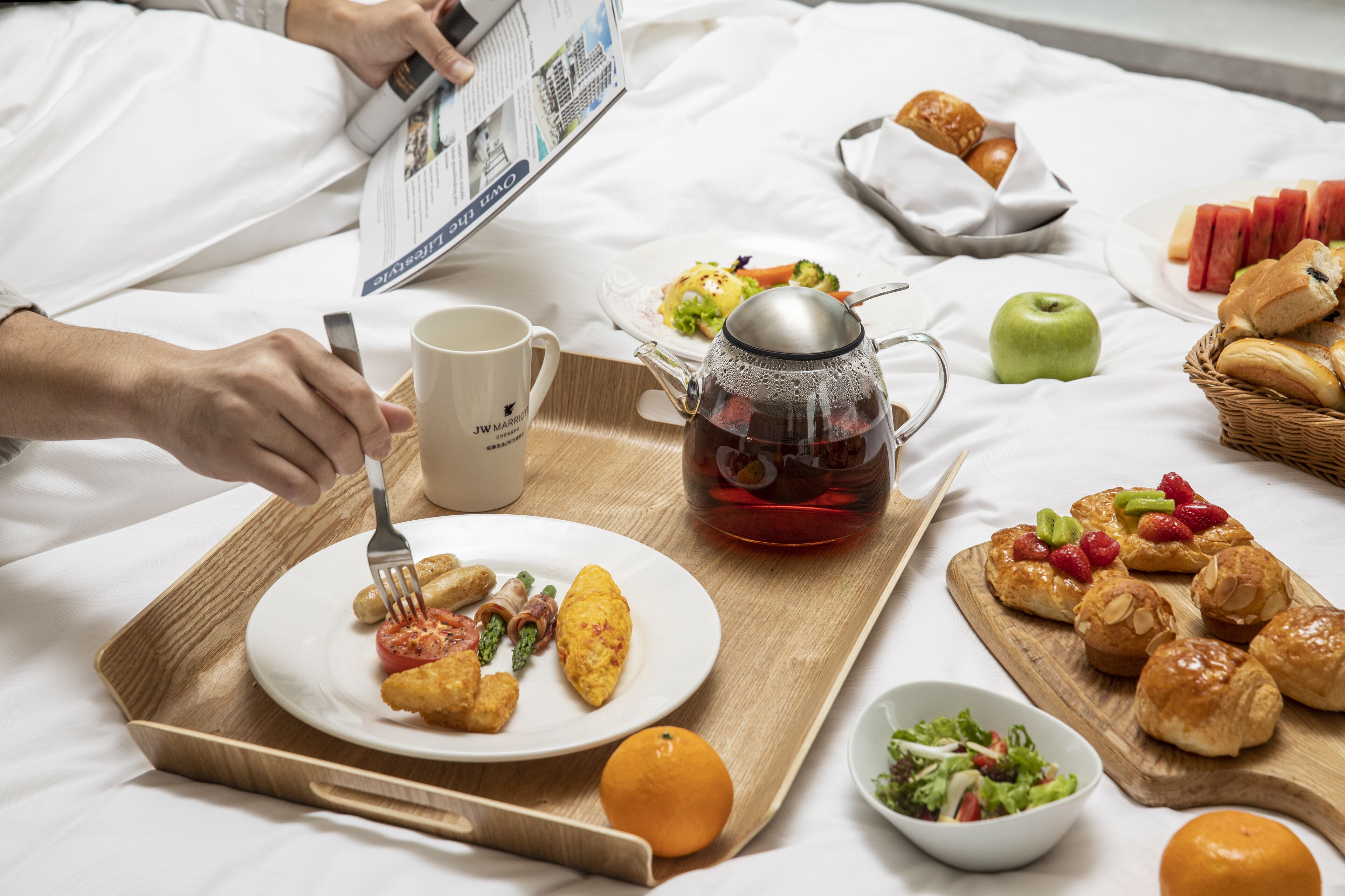 Una bandeja de desayuno con cruasanes, un set de té y un plato de comida que incluye huevos y tomates.