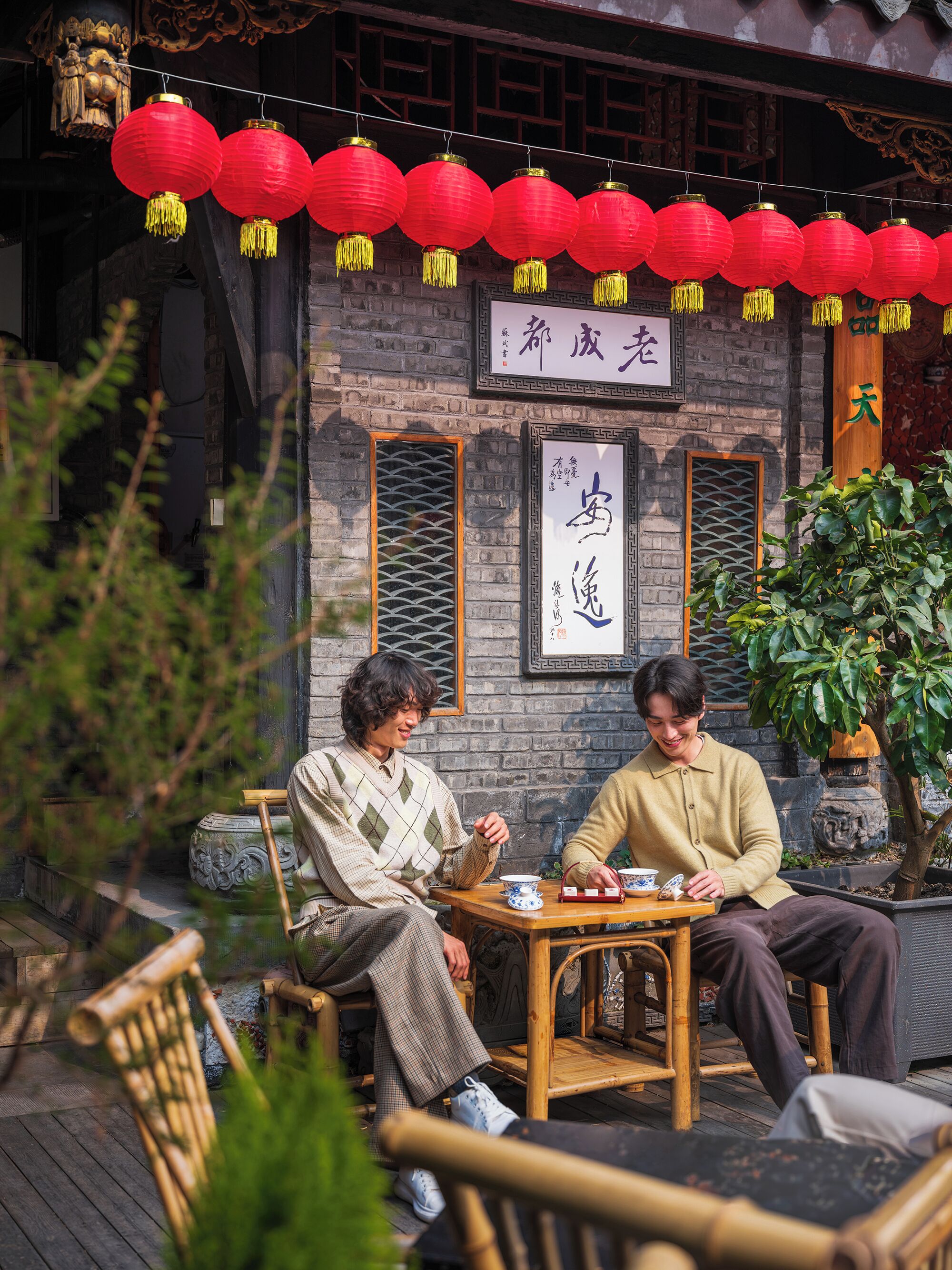 Deux personnes sont assises à une table à l’extérieur d’un bâtiment à l’architecture chinoise traditionnelle, sur lequel on peut voir une enseigne avec des caractères chinois.
