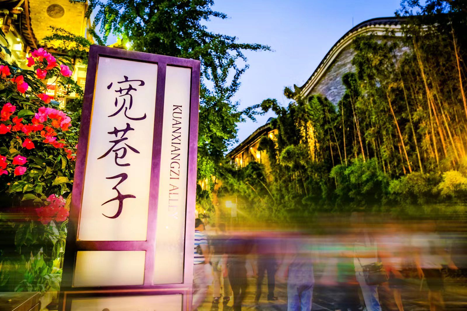 A sign with Chinese characters, a building with traditional architecture, and a blurred background of people.