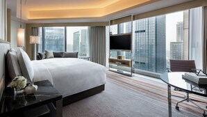 Une chambre d’hôtel moderne dotée d’un grand lit, d’un bureau, d’une chaise, d’une télévision et d’une grande fenêtre donnant sur la ville.