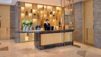 A hotel reception area with a marble counter, modern lighting, and a receptionist.