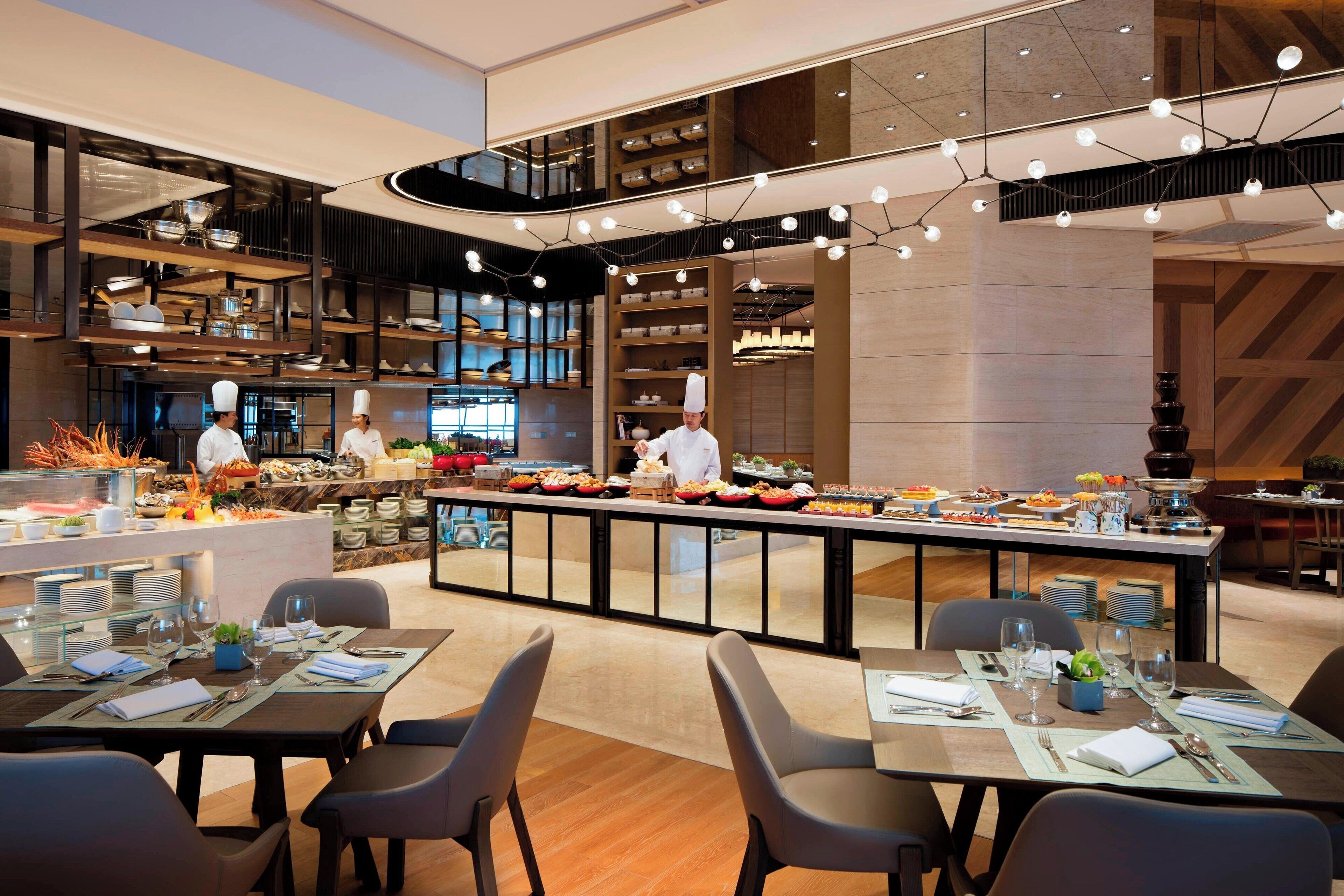 Un restaurante moderno con una zona central de servicio, varias mesas para comer y un chef preparando comida.