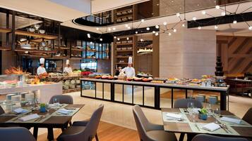 Un restaurante moderno con una zona central de servicio, varias mesas para comer y un chef preparando comida.