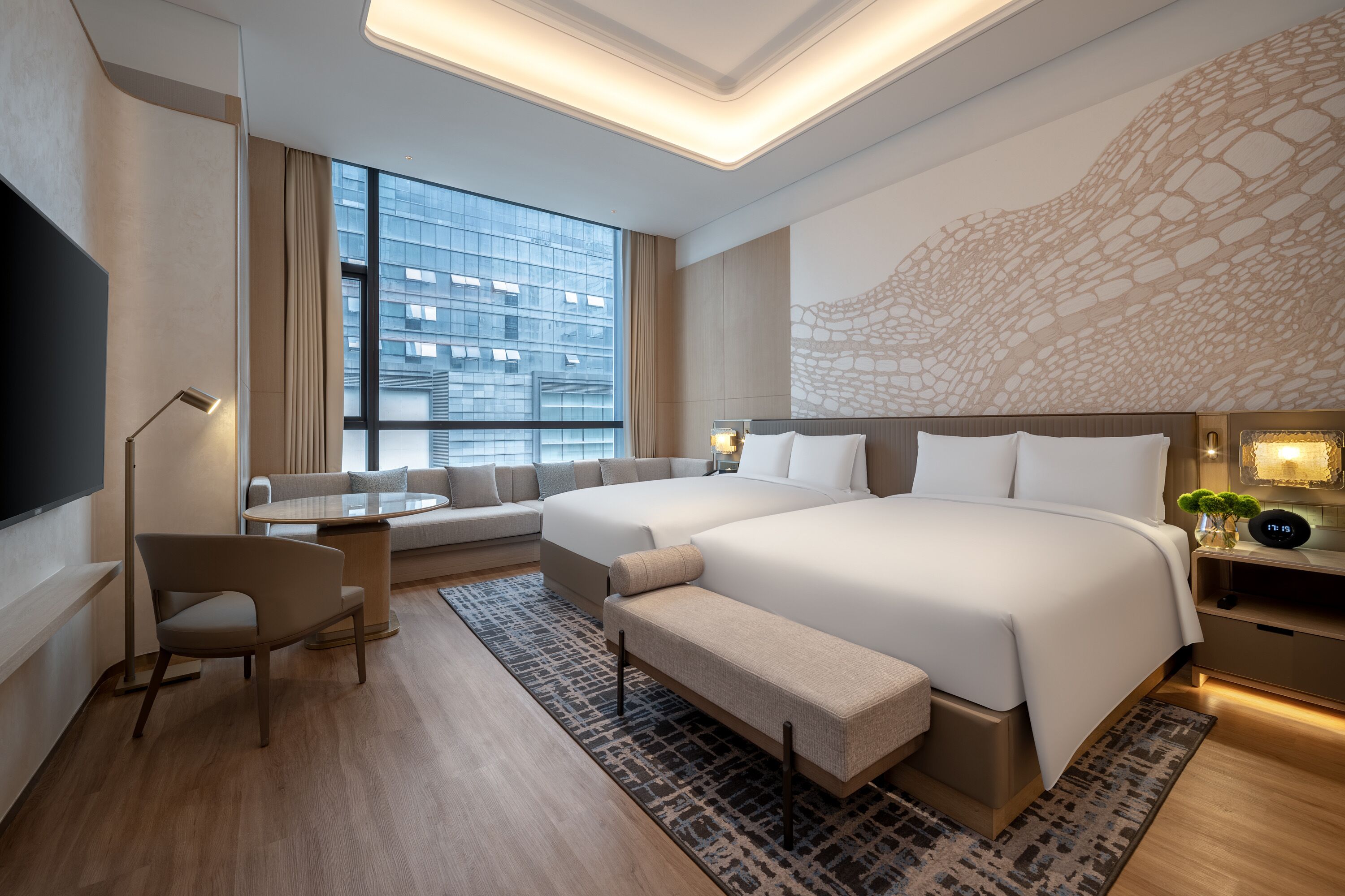 A modern hotel room with a large bed, a sofa, a desk, and a TV.