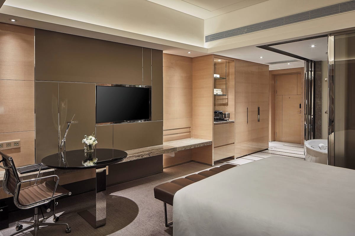 Una habitación de hotel moderna con una cama grande, un escritorio con una silla, un televisor de pantalla plana y un baño con bañera y ducha.
