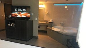 Ein Hotelzimmer mit Fernseher, der '10 PIEZAS' zeigt, einer Minibar, einem Badezimmer mit Badewanne und Dusche.
